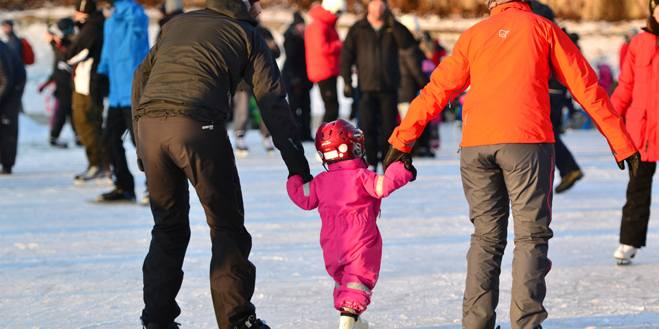 Barn och vuxna som åker skridsko på en solig isbana. Foto Petra Sundström .